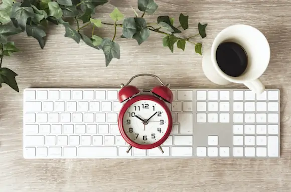 Keyboard, red alarm clock and coffee cup on a desk